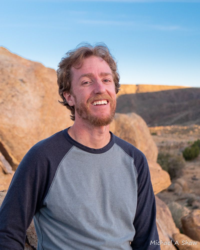 James Simpson smiling outdoors in front of desert boulders and rock formations