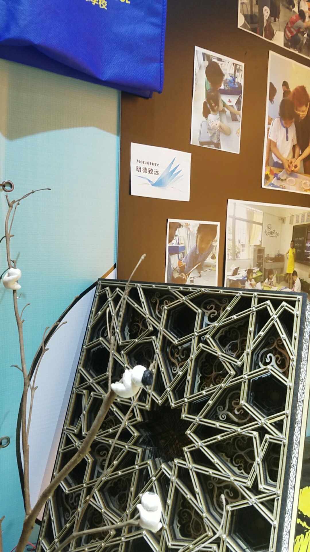 A laser-cut geometric wood panel displayed near photos of students building electronics