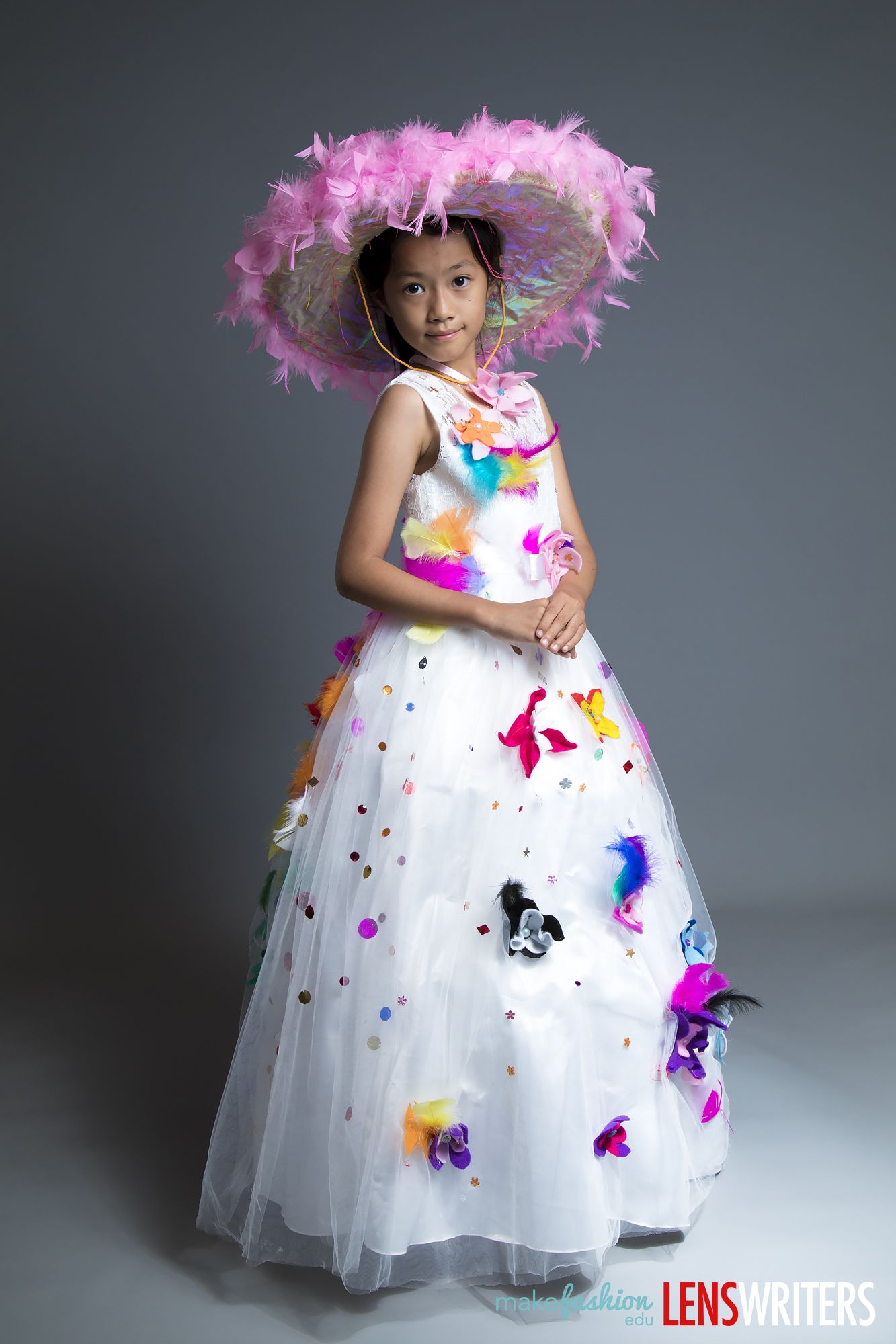 Student models a flower-covered quinceañera dress with a wide feathered hat