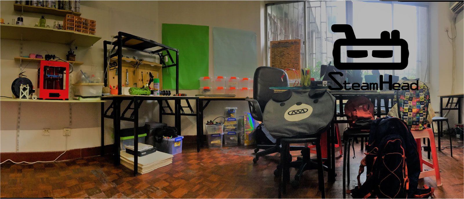 SteamHead makerspace interior with 3D printer, workbenches, and the SteamHead logo