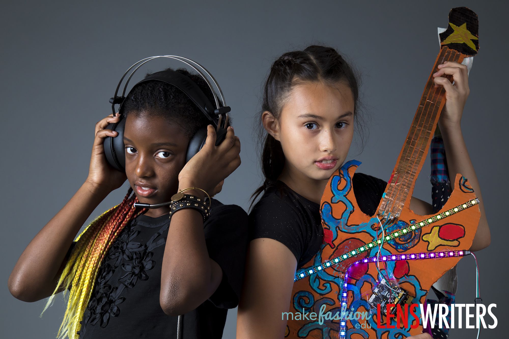 Two students posing with a light-up cardboard guitar and headphones