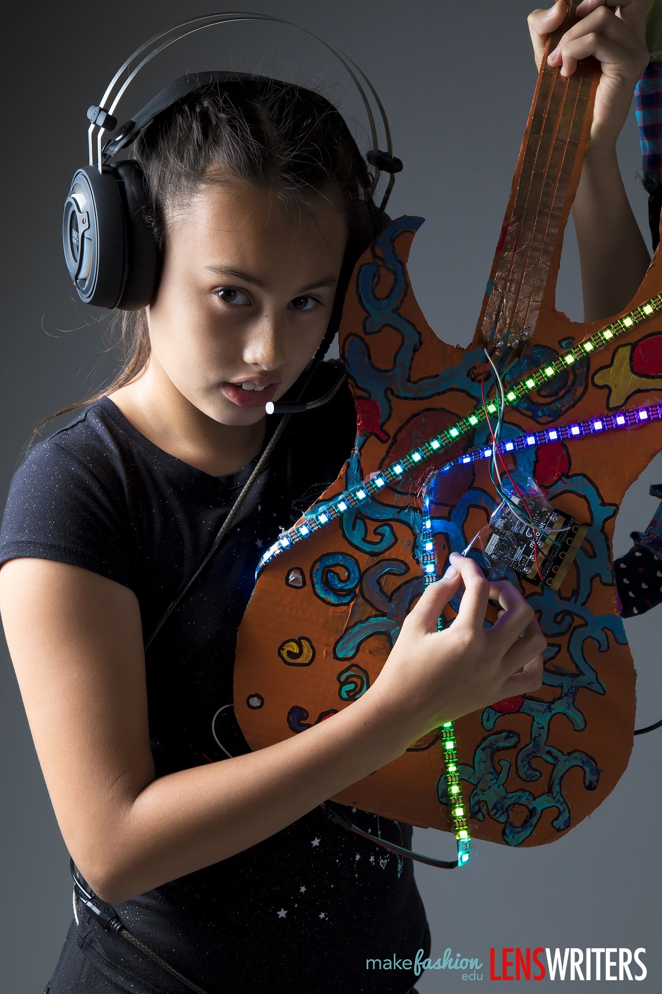 Student wearing headphones beside the glowing guitar neck