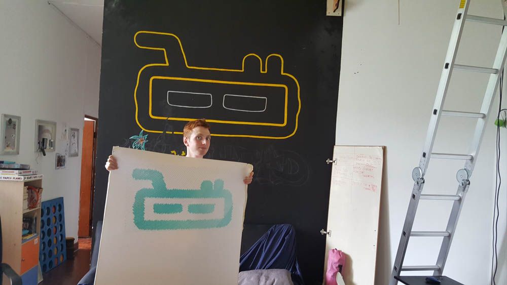 Oliver Child holding up a large paper template in front of a chalkboard mural