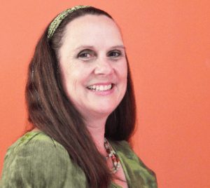Twila Busby smiling in a portrait against an orange background