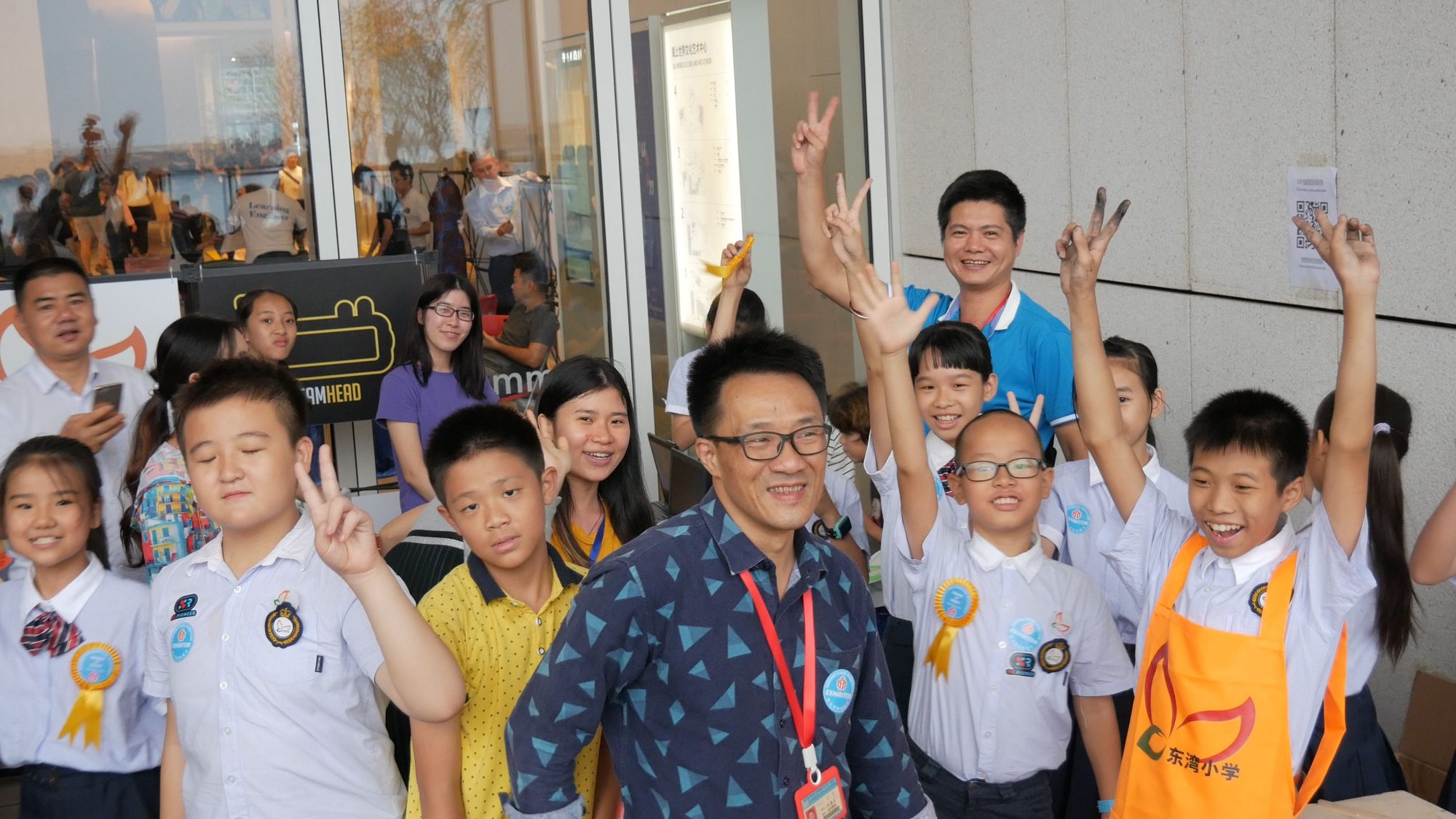 Group of students and teachers waving at a Maker Faire booth