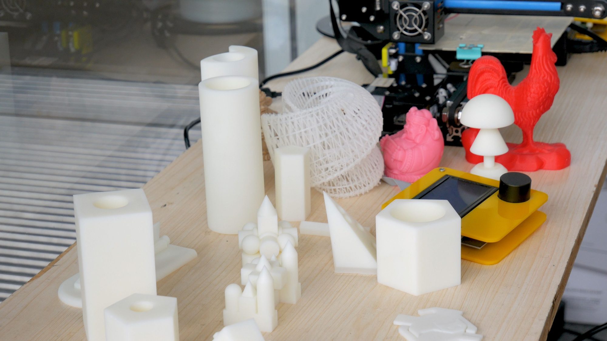 3D-printed rooster, candle holders, and shapes displayed on a workbench