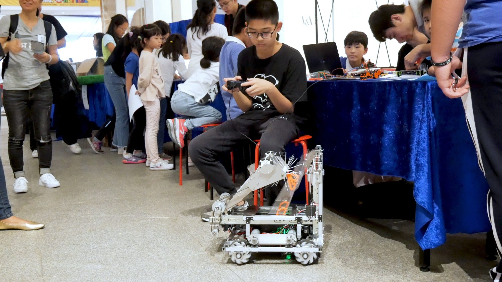 A student drives a wheeled robot with a remote control at a maker faire booth