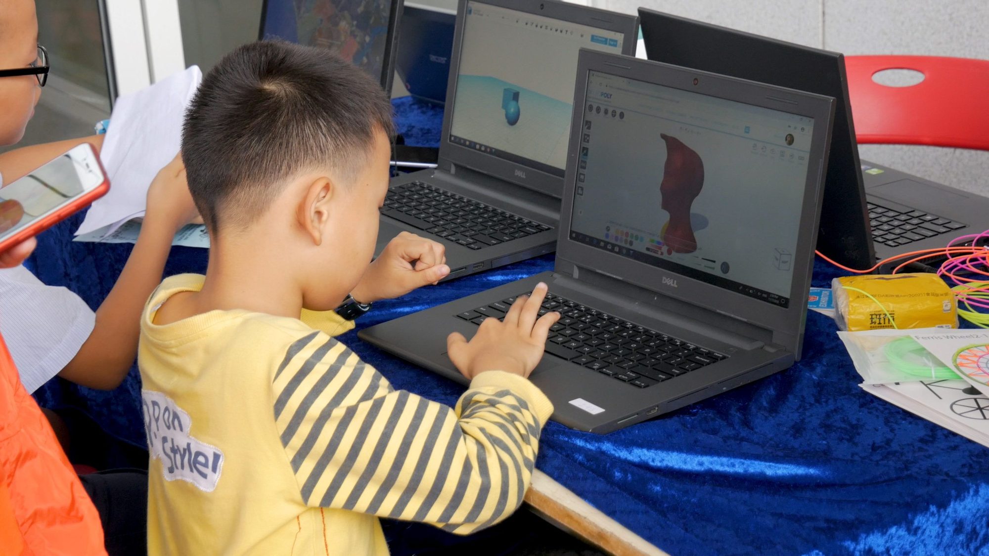 A student sculpts a 3D model on a laptop at an outdoor table