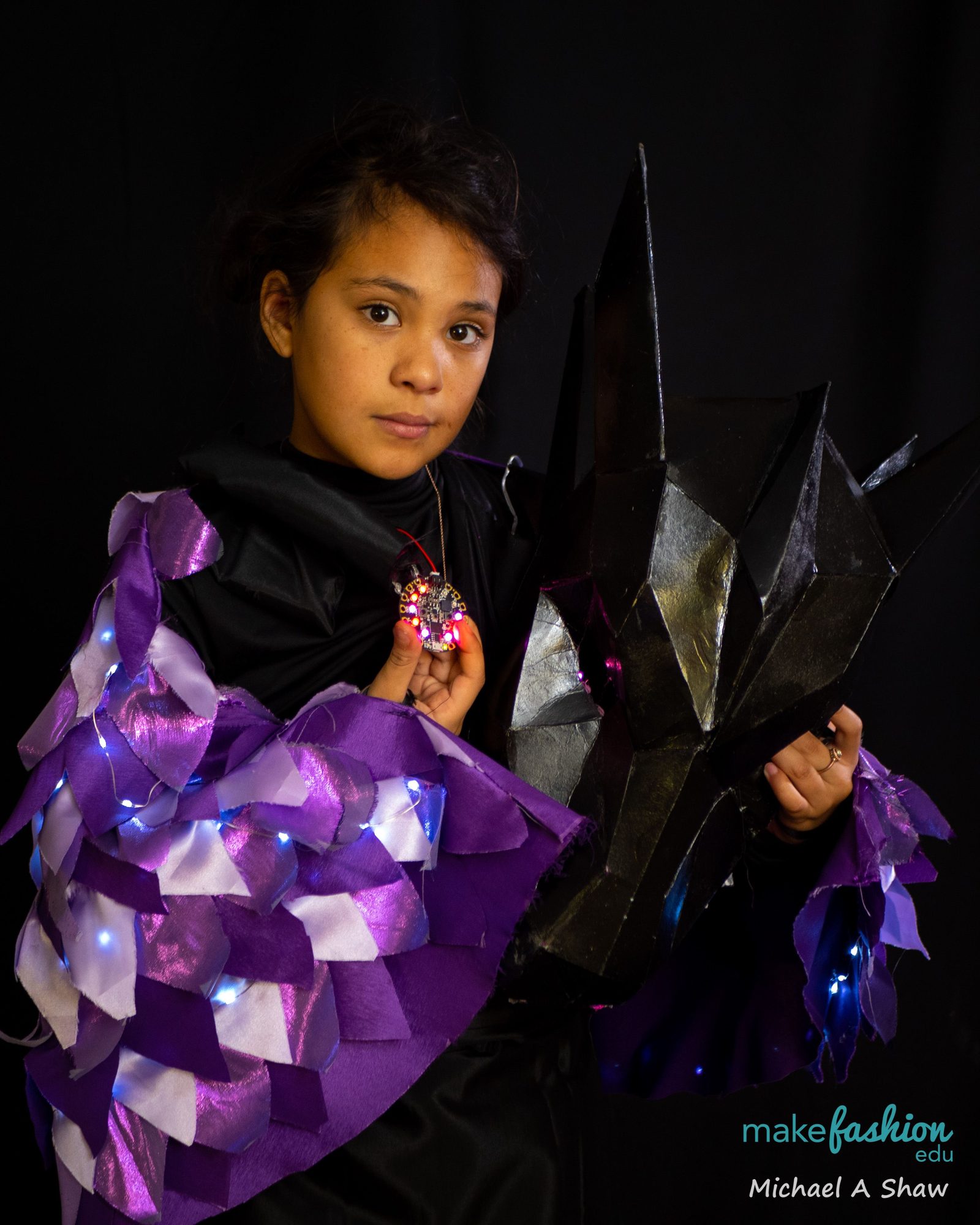 Student in purple LED scale wings holds a glowing circuit board pendant