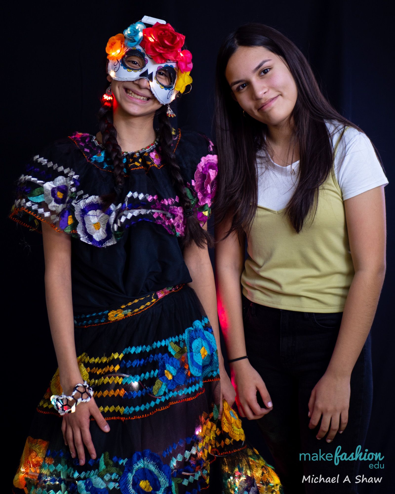 Two students, one in an illuminated sugar skull mask and dress