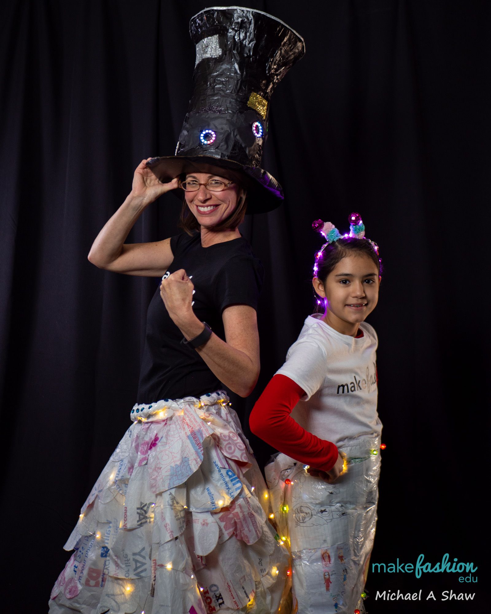 Woman in a tall light-up top hat posing beside a student in an LED headband
