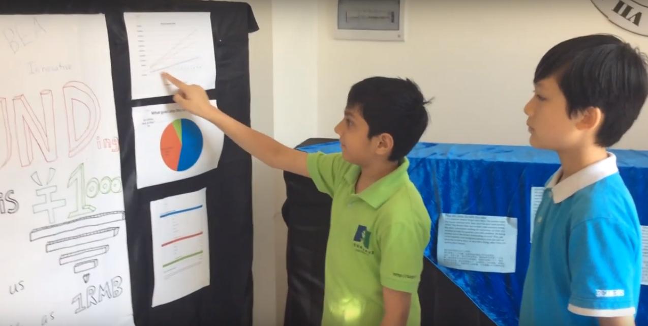 Two students review funding charts on a project poster at a school fair