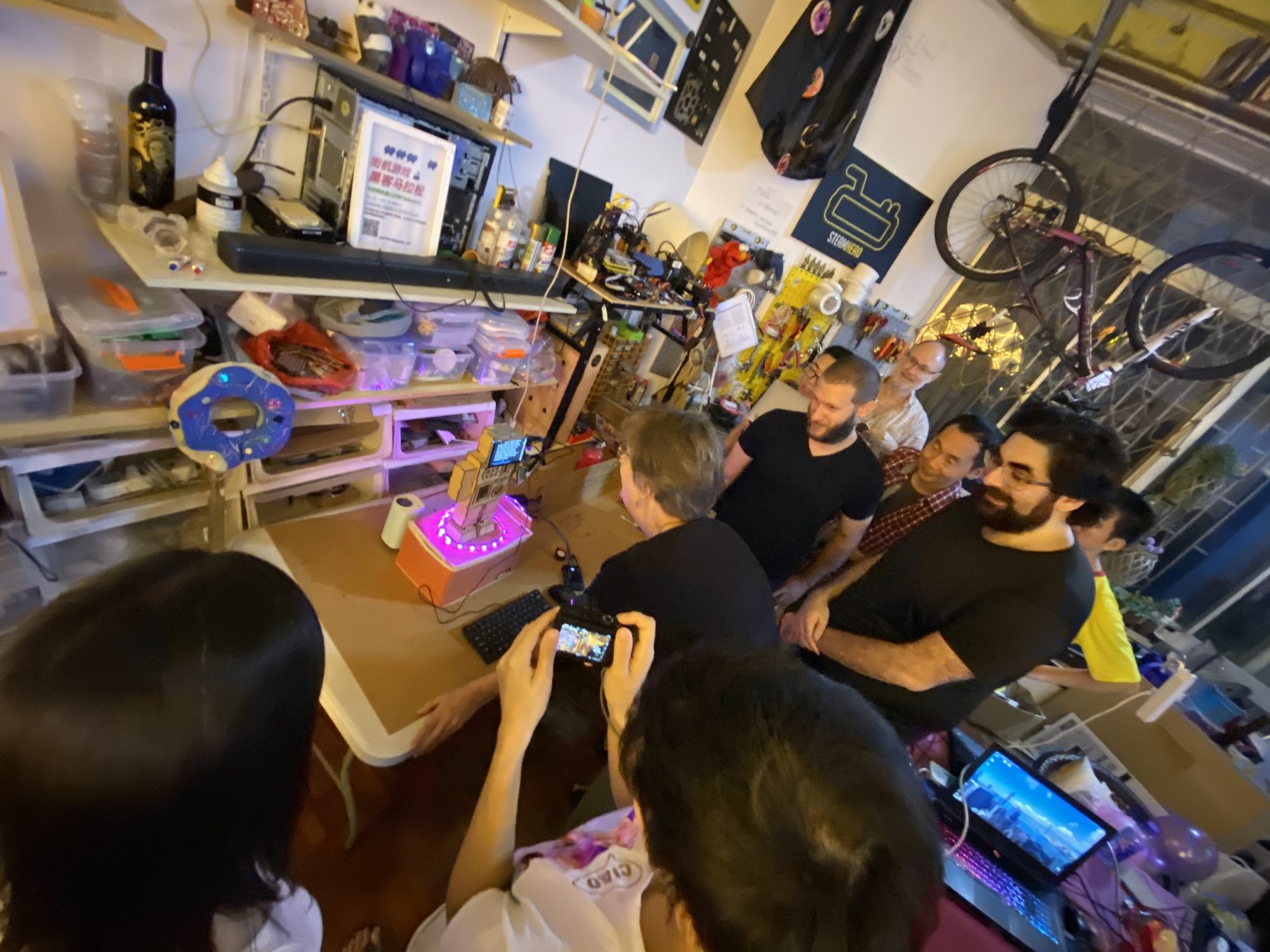 Group gathered around a glowing pink LED sculpture on a workbench