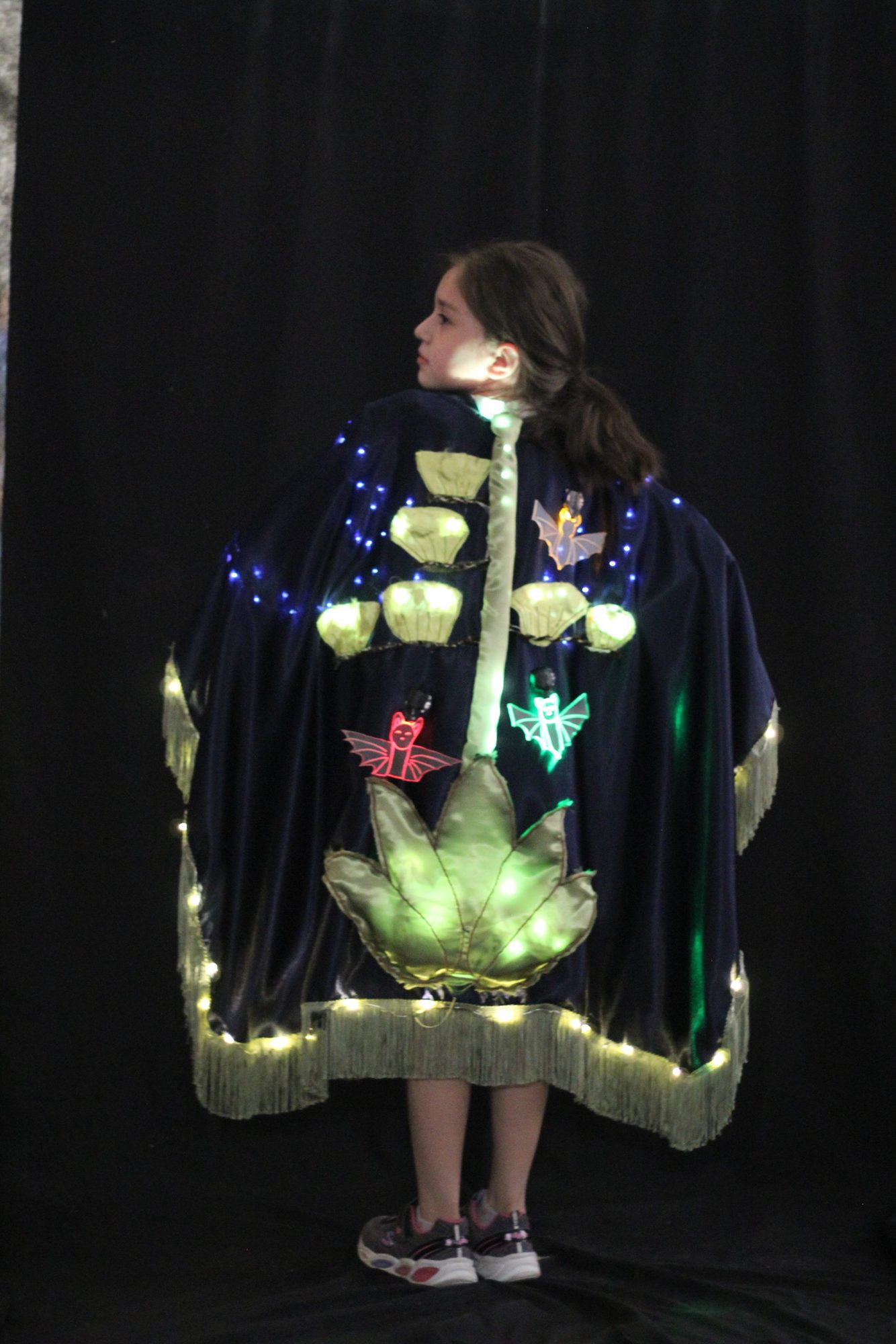 Student wearing a navy cape with illuminated bat and leaf appliques
