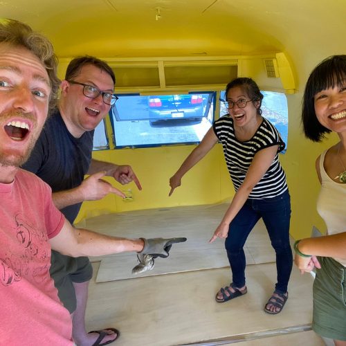 Mobile Makerspace chapter 10: four volunteers posing and pointing inside the newly yellow-painted trailer interior