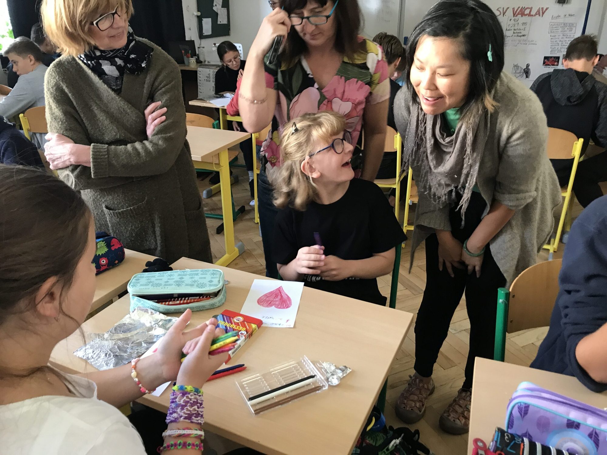 Educators and a student sharing a laugh over colored-pencil artwork in class