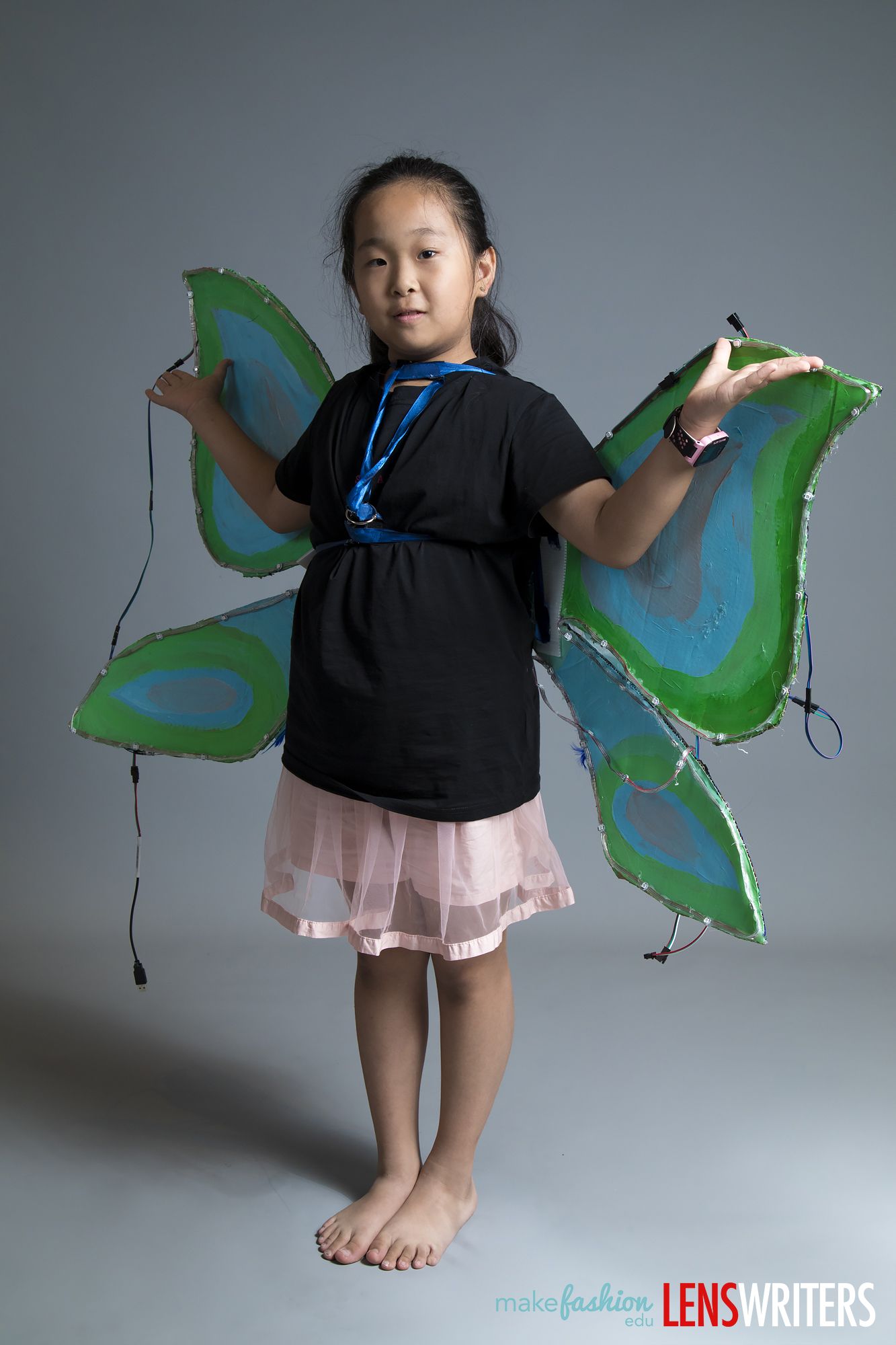 Student model wearing LED-embellished green butterfly wings with blue pattern detail