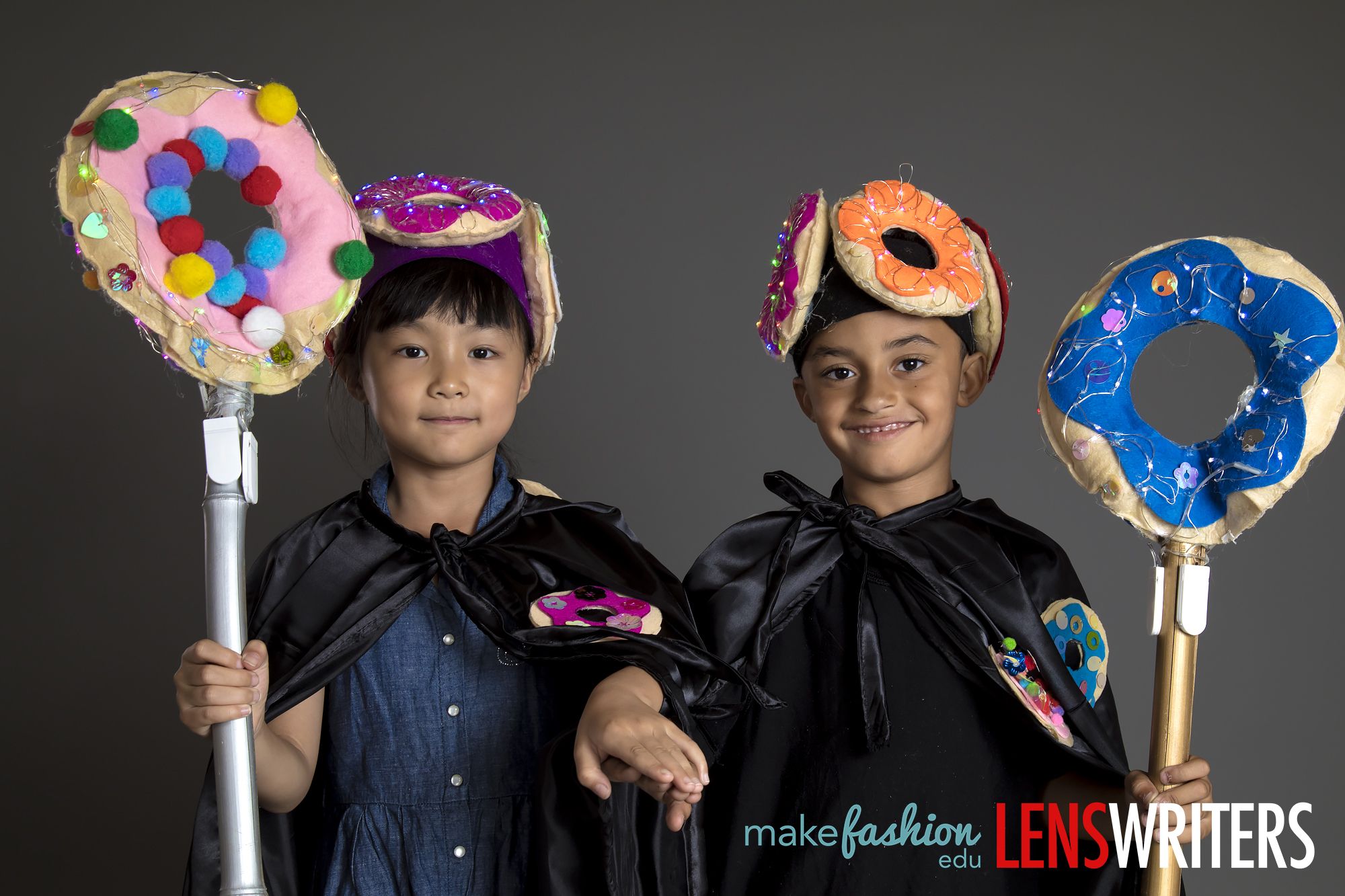 Student designers holding oversized illuminated lollipop-shaped headdresses with colorful pompoms