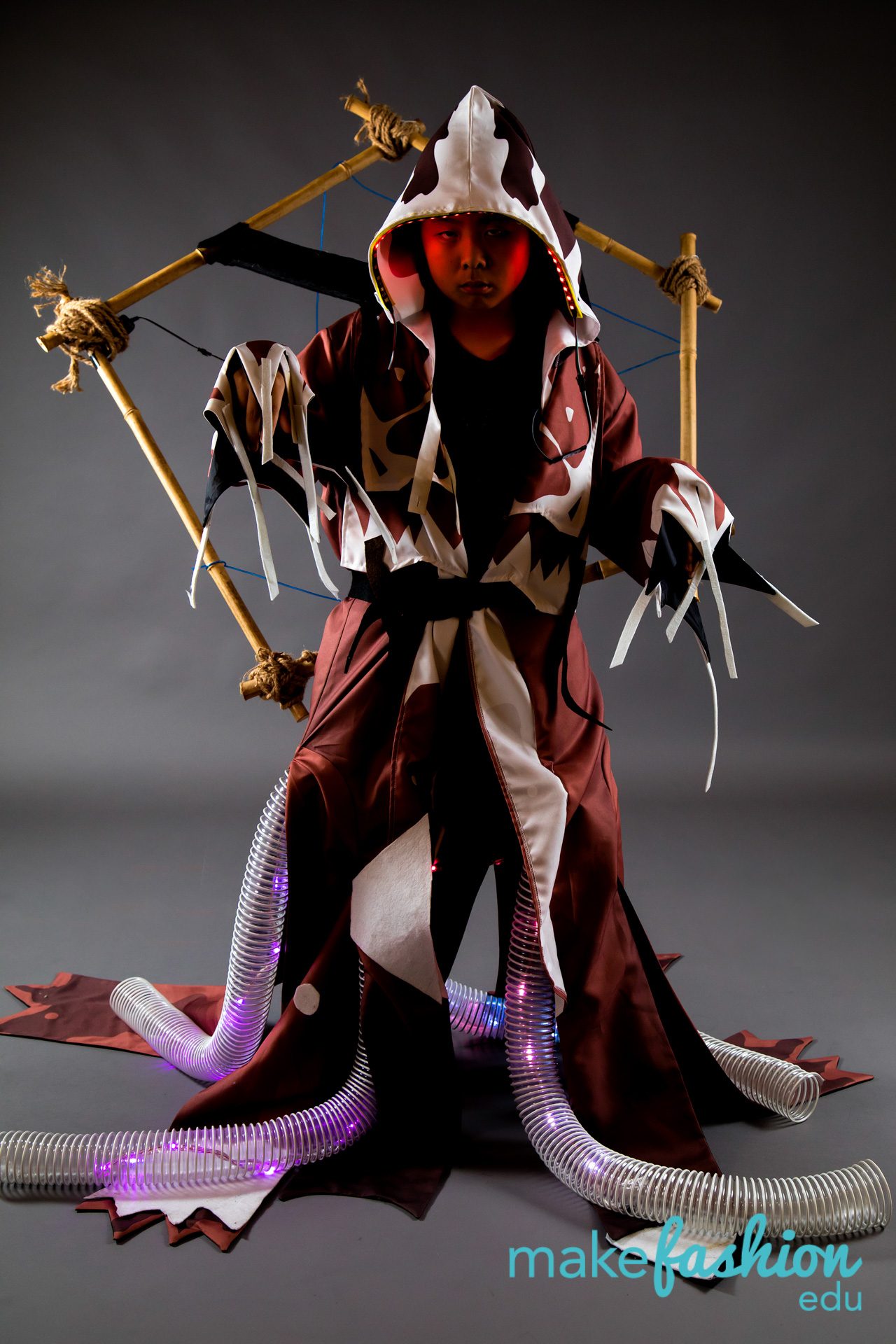 Student model in tattered robe with red LED-lit hood and purple LED tubing at feet