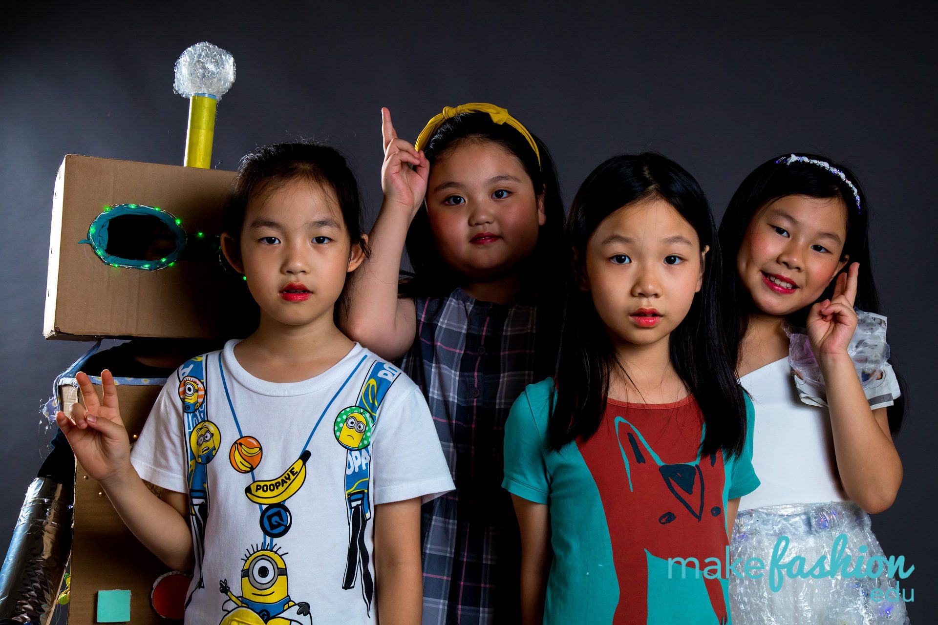 Group of young models posing beside a cardboard robot costume with an LED eye