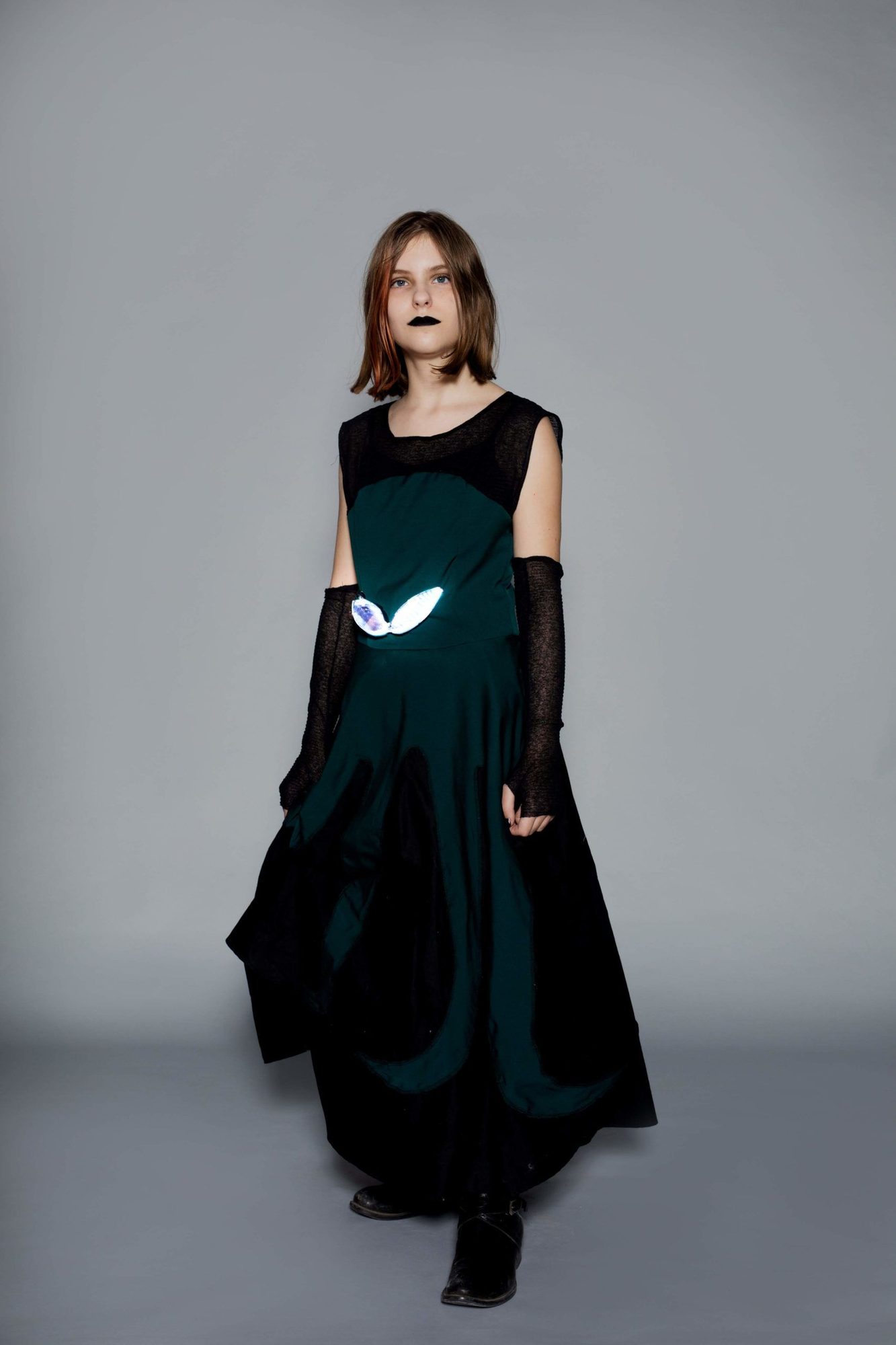 Student model in teal and black dress with glowing white eye-shaped LED wearable on chest and black mesh gloves
