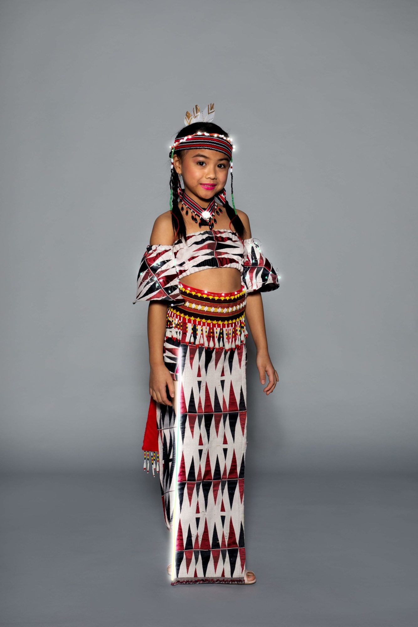 Student model in patterned crop top and skirt with feather headband and glowing LED trim
