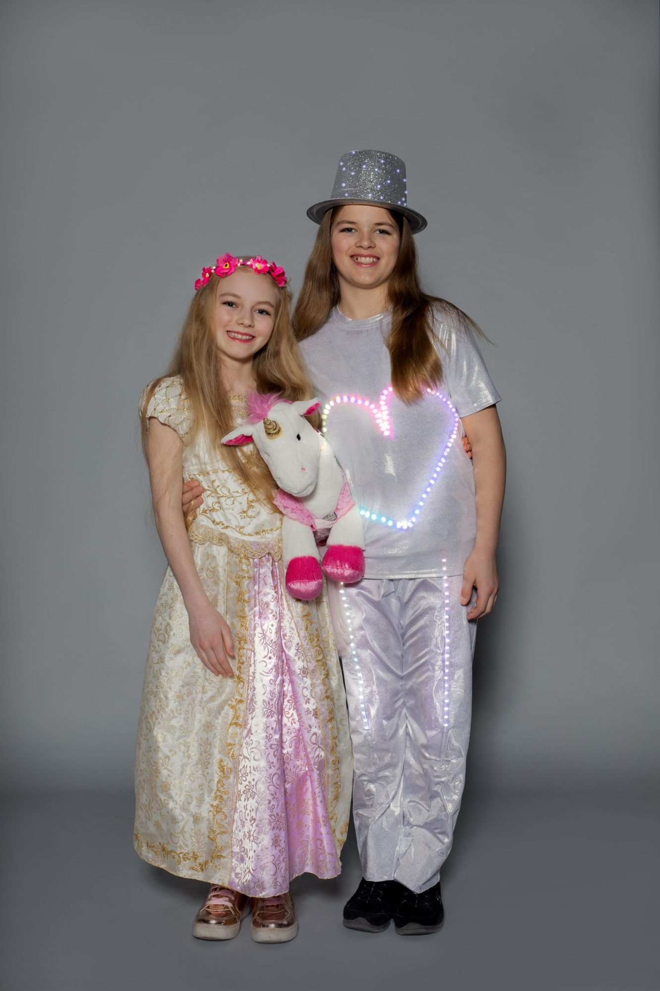 Two student designers, one in gold dress with flower crown, other in LED heart shirt