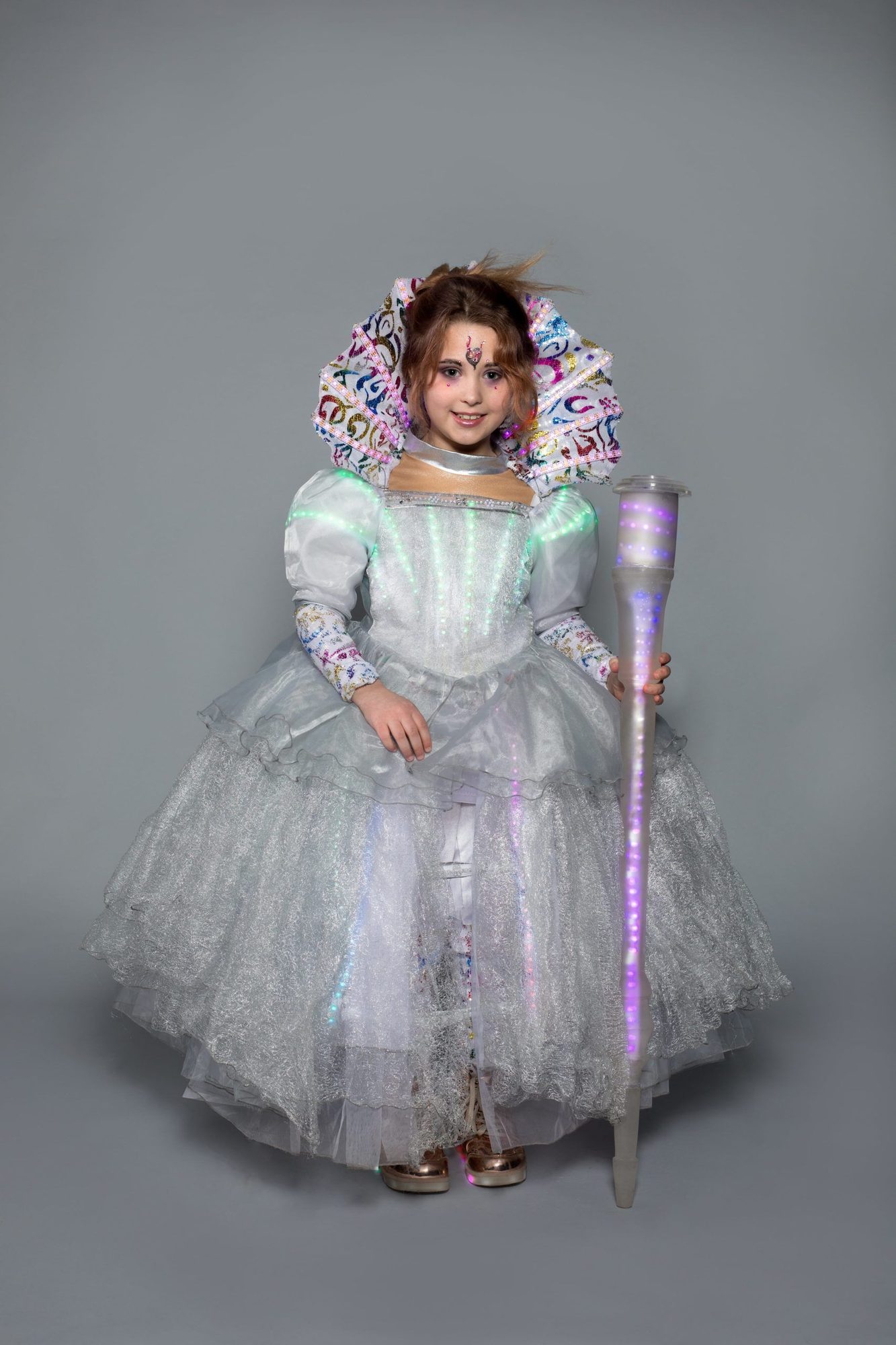 Student model in sparkly white princess dress with multicolored fan-shaped headpiece and glowing LED baton