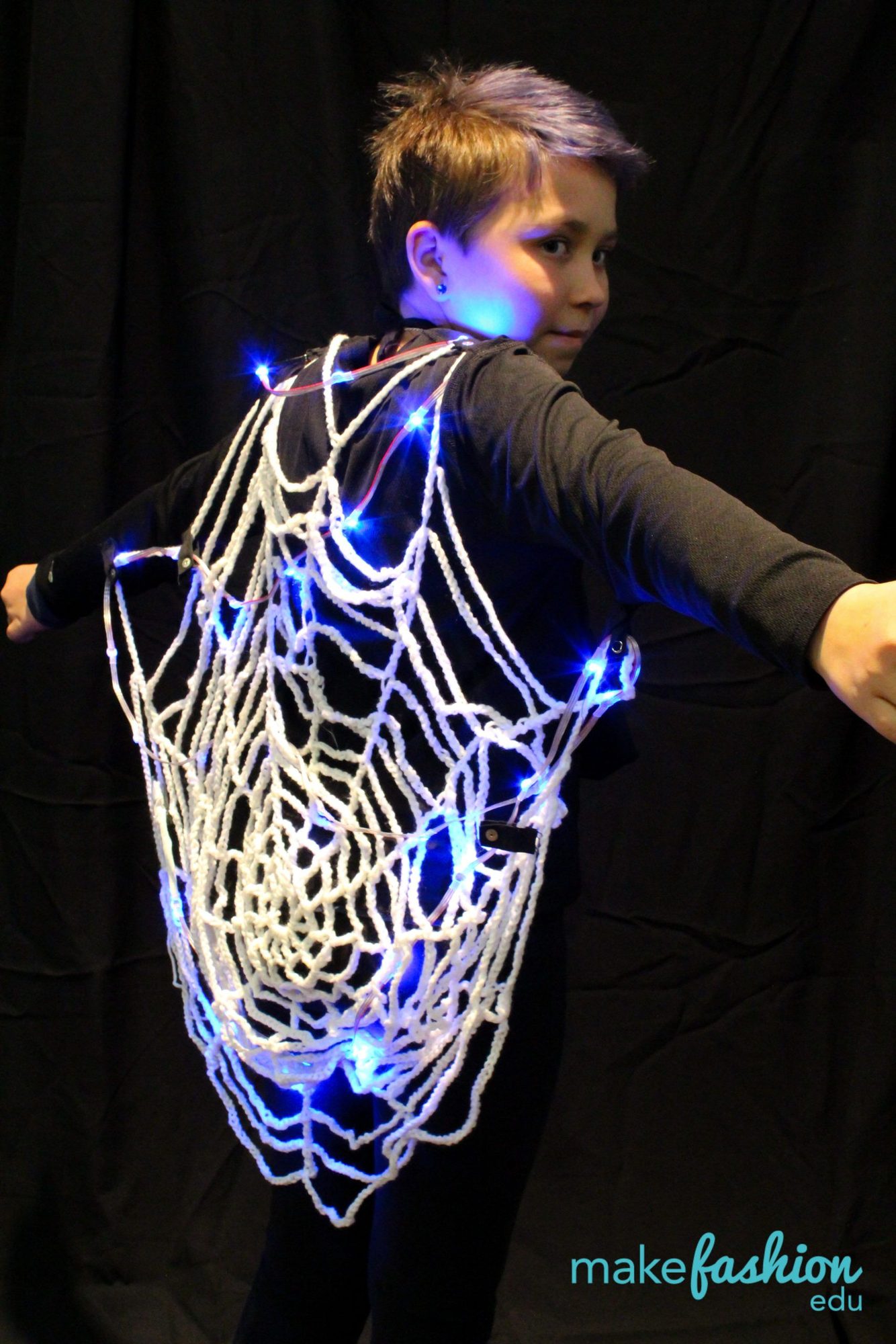 Student model in a crocheted web cape lit with scattered blue LEDs