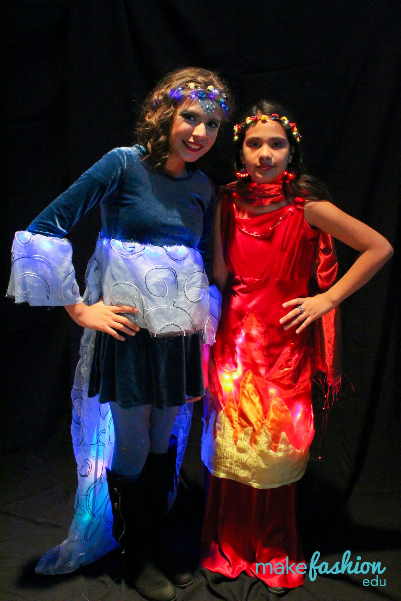 Two student models in blue and red LED-lit gowns with flower crowns
