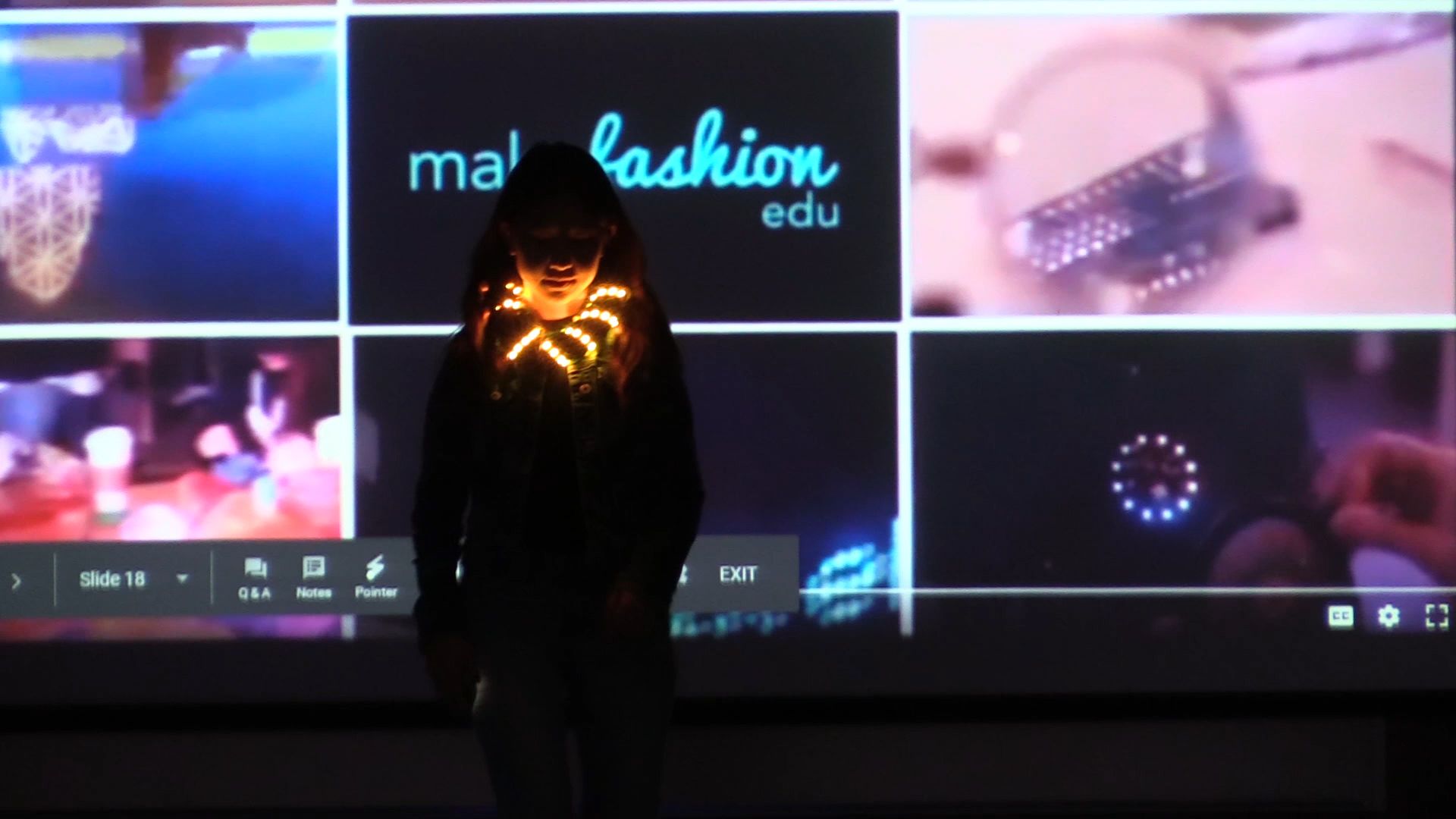 Student on runway holding glowing amber LED ornament with slideshow backdrop