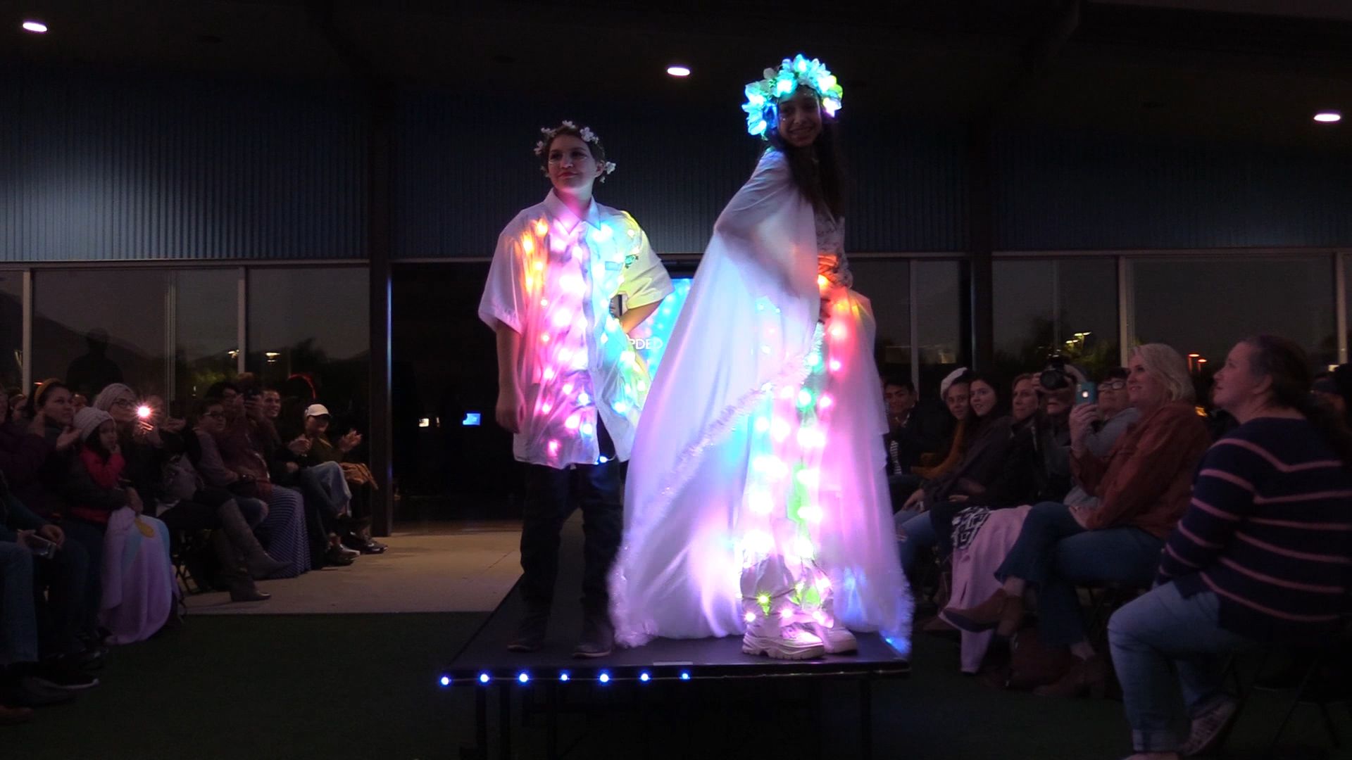 Two students modeling white garments with multicolor LED lights on runway