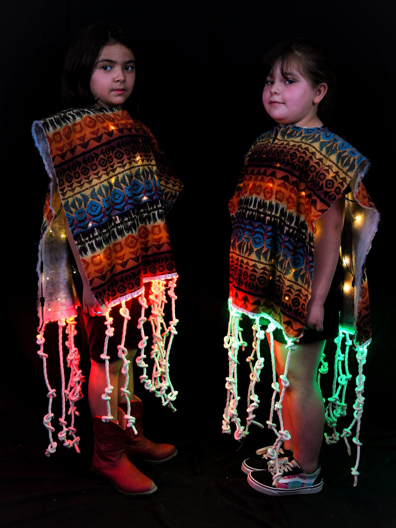 Two students wearing patterned vests with colorful LED strings hanging down