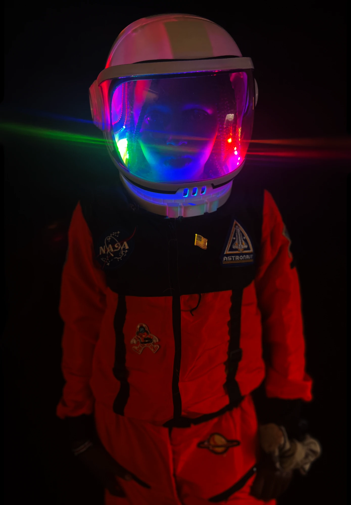 Student in an orange astronaut suit wearing a space helmet lit inside with rainbow LEDs